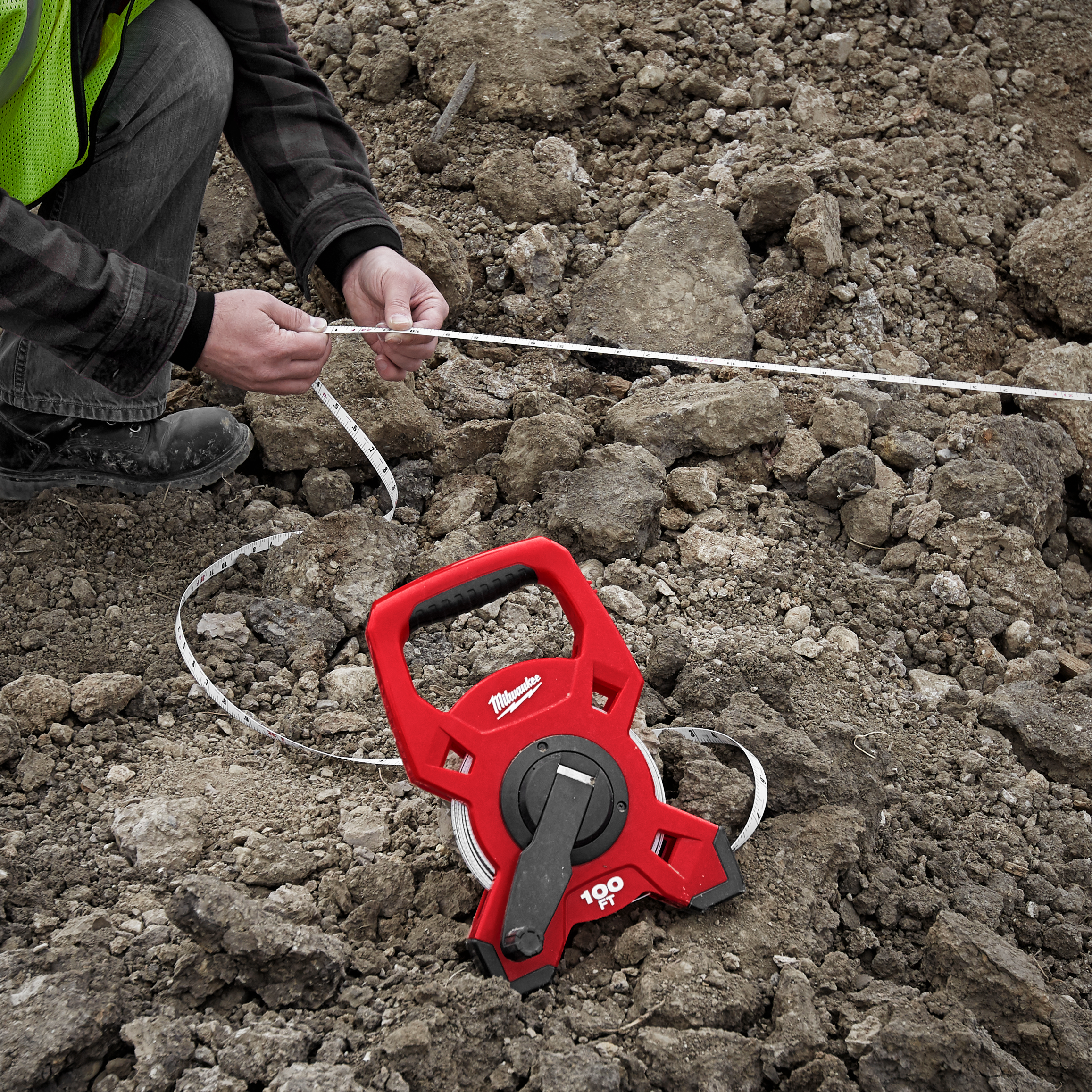 Person using a red tape measure on rocky ground