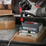 Hand wearing a glove using a screwdriver on a power inverter with a blurred background