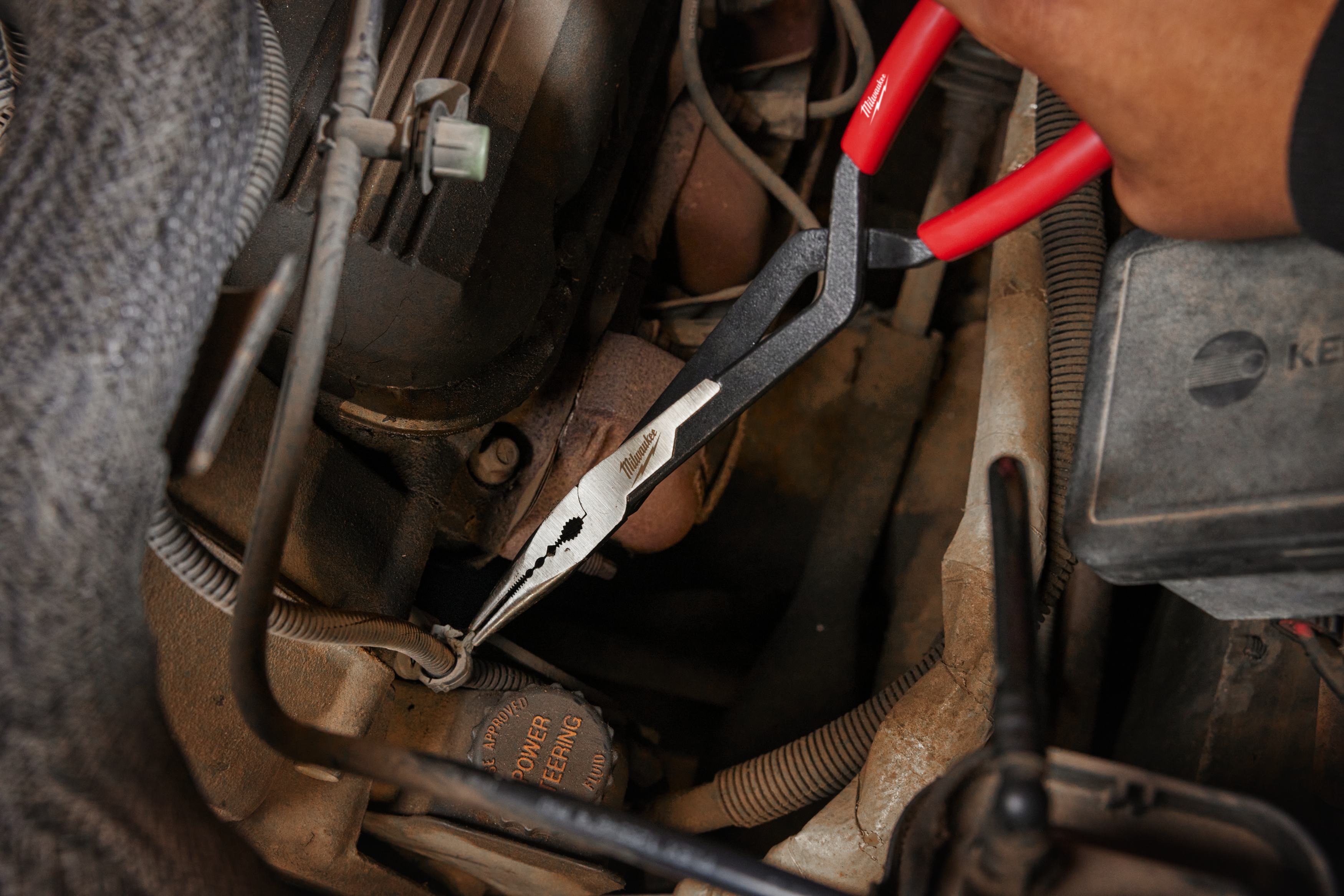 Close-up of long reach pliers inside engine bay.