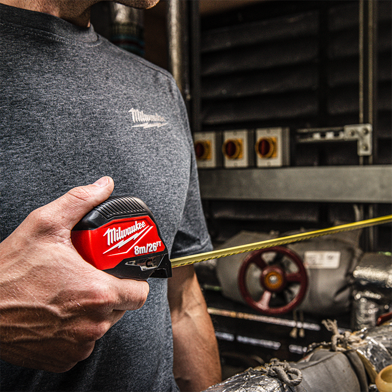 Person holding a Milwaukee tape measure with an industrial setting  background