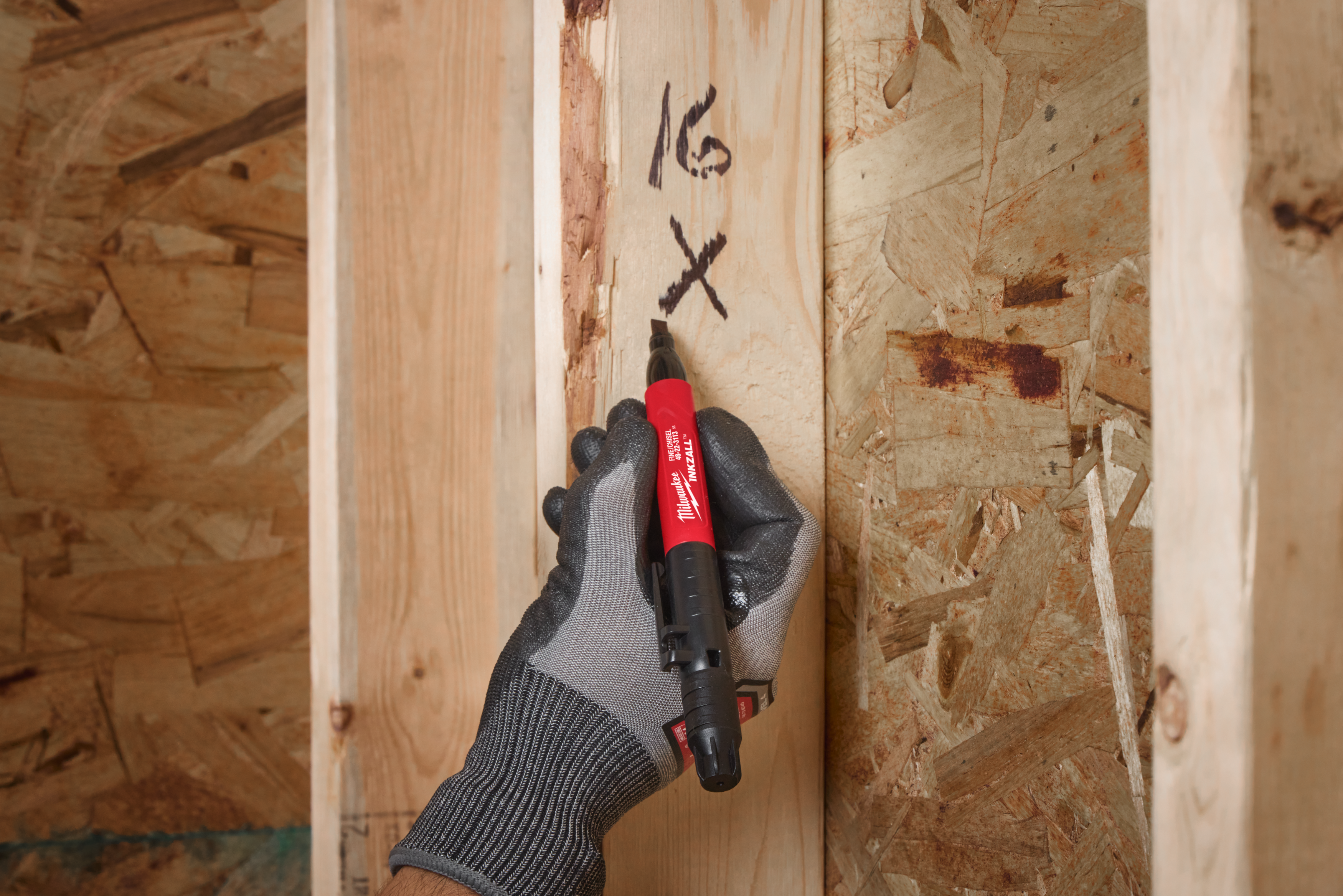 Hand wearing a glove holding a red marker on a wooden surface