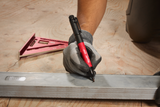 Person using a pen on a metal strip with a square ruler and pencil on a wooden surface