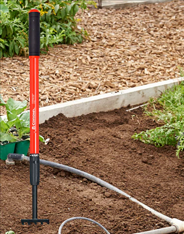 Red and black garden tool with a hose on a garden bed