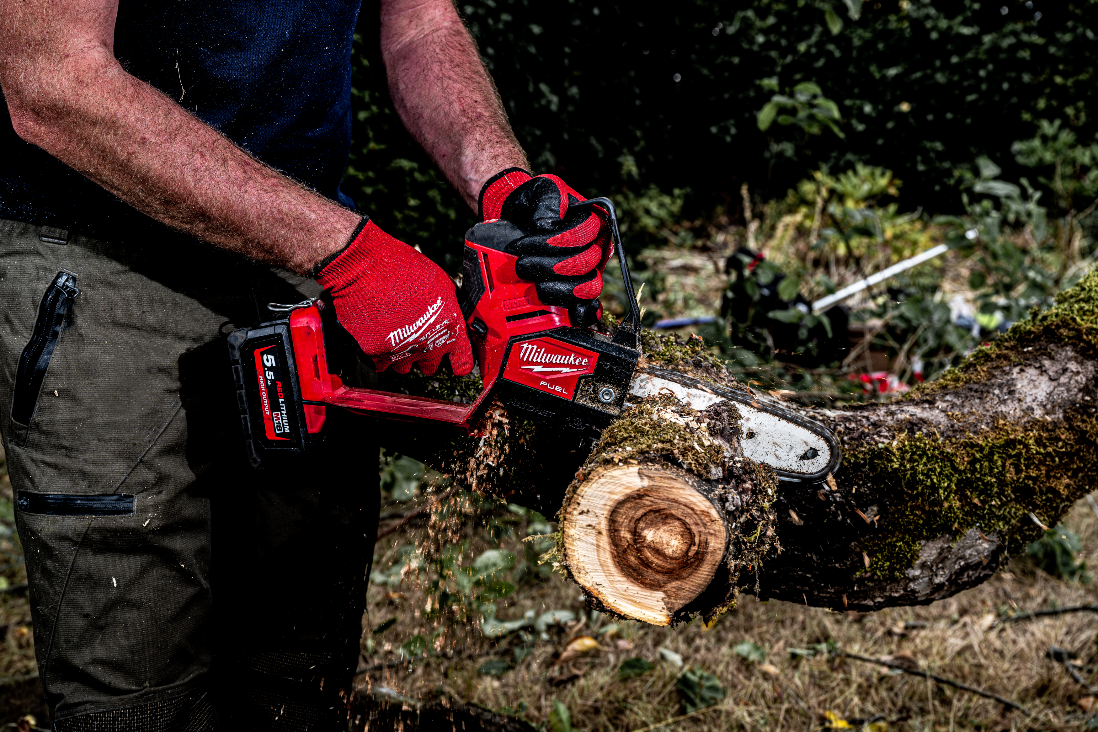 Person using a Milwaukee power tool to cut a log outdoors