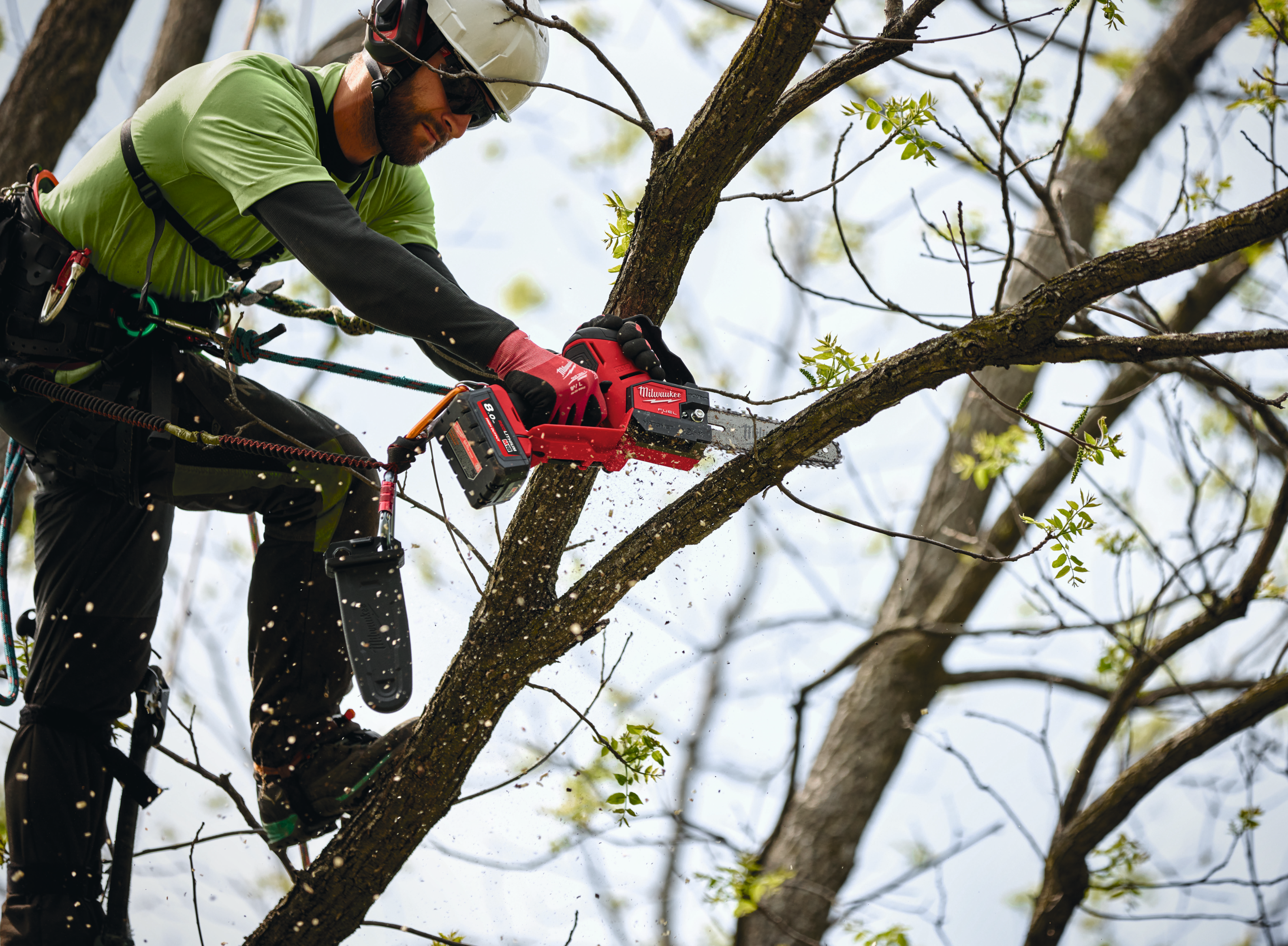Person trimming a tree branch with a chainsaw, wearing safety gear.
